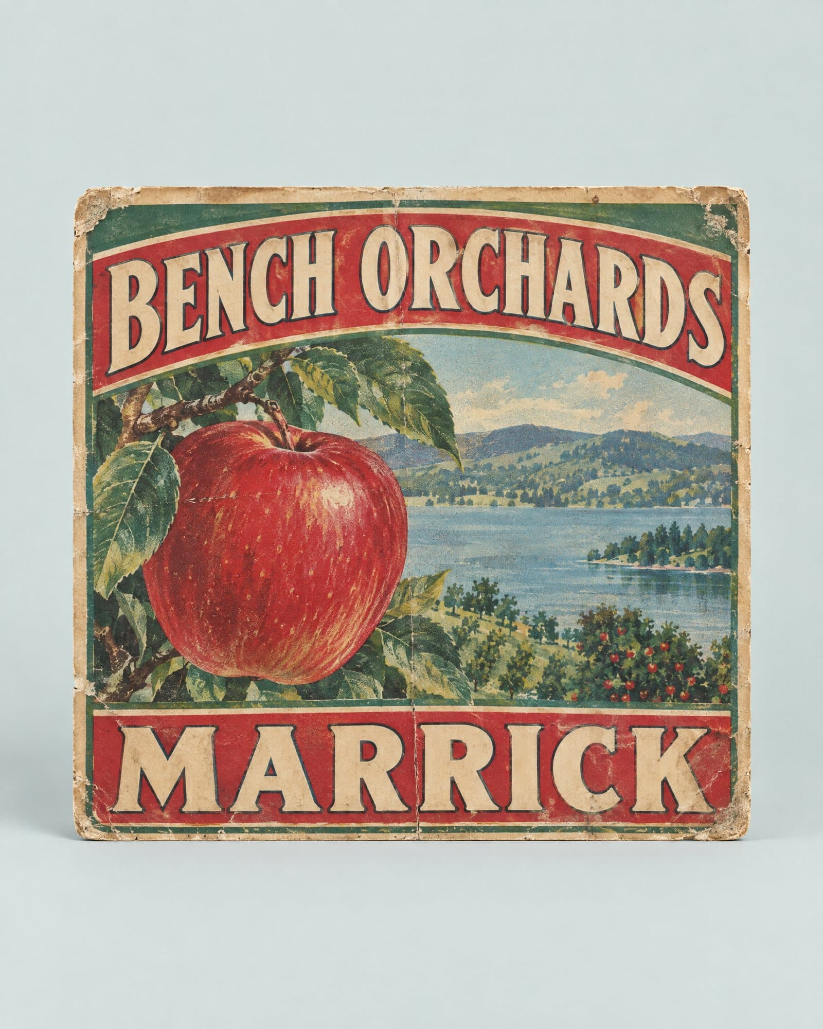 An apple crate label with a red apple, the lake and orchard hills, reading Bench Orchards, Marrick.