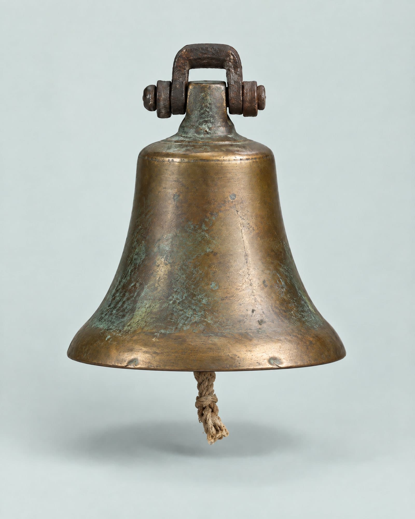 A heavy bronze ship's bell with a green patina and a short rope pull hanging from the clapper.