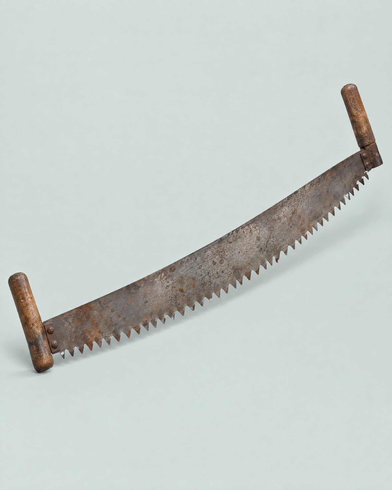 A long two-man crosscut saw with a wooden handle at each end and rusted teeth.