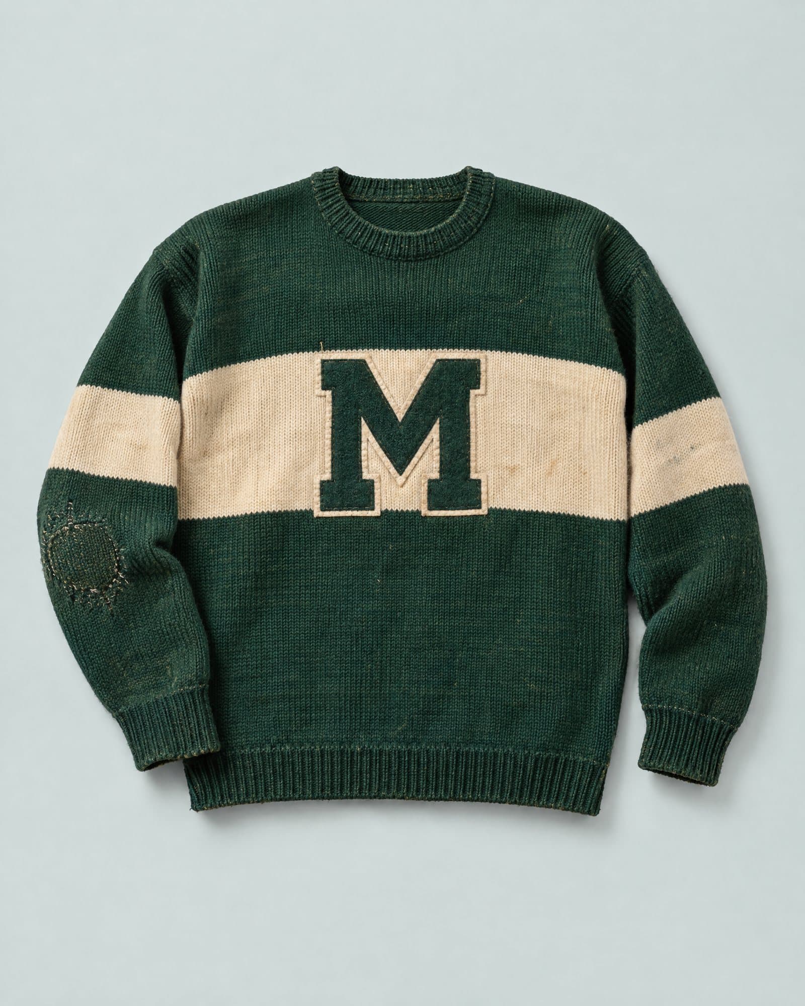 A green knit hockey sweater with a cream stripe and a green M, one elbow darned.