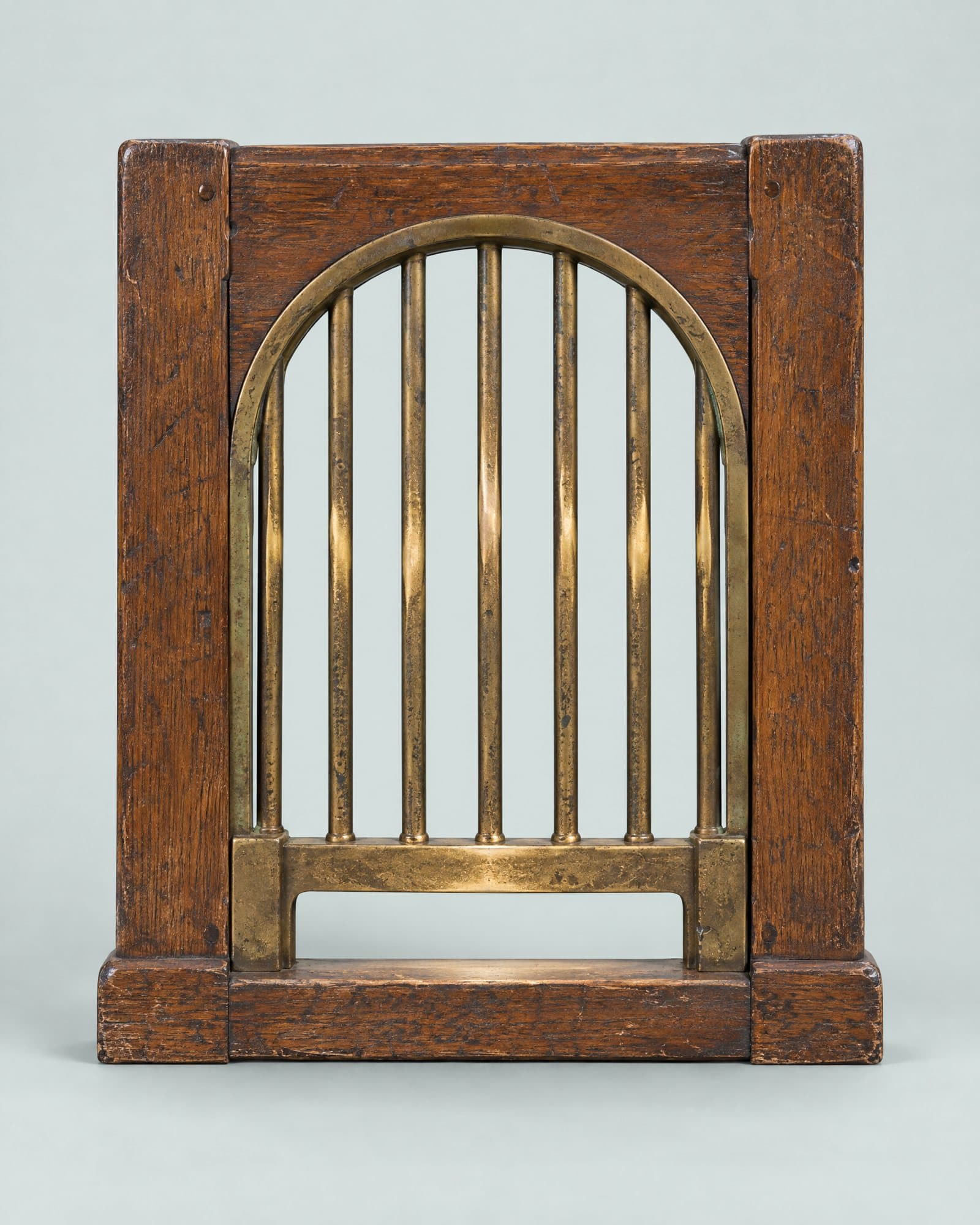 An oak post office wicket with an arched brass grille, the brass worn bright along the bottom.